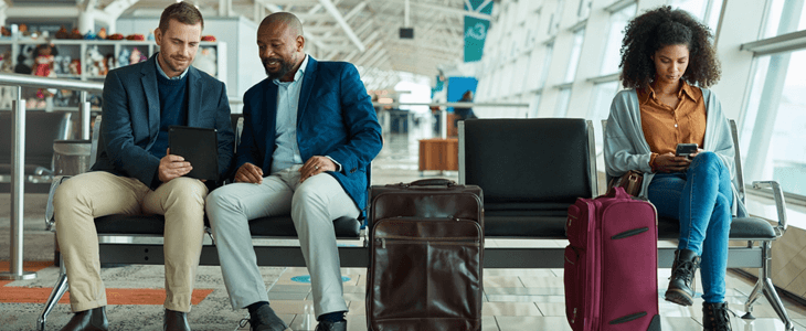 three people with luggage sit on an airport bench 